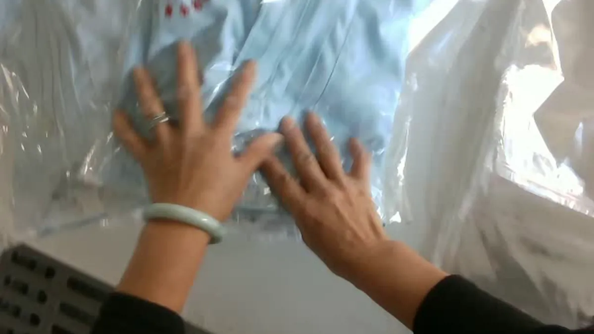Low-resolution head-mounted view of hands smoothing a folded shirt in a plastic bag