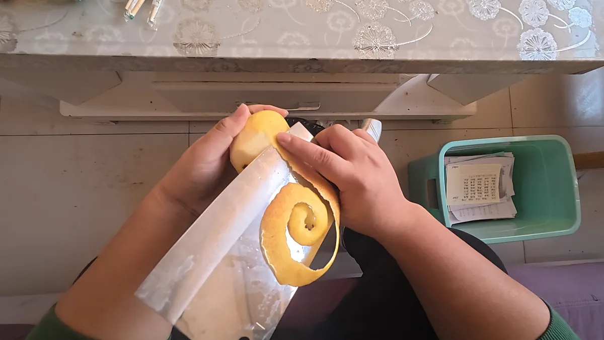 Head-mounted view of bare hands peeling a pear over a bin