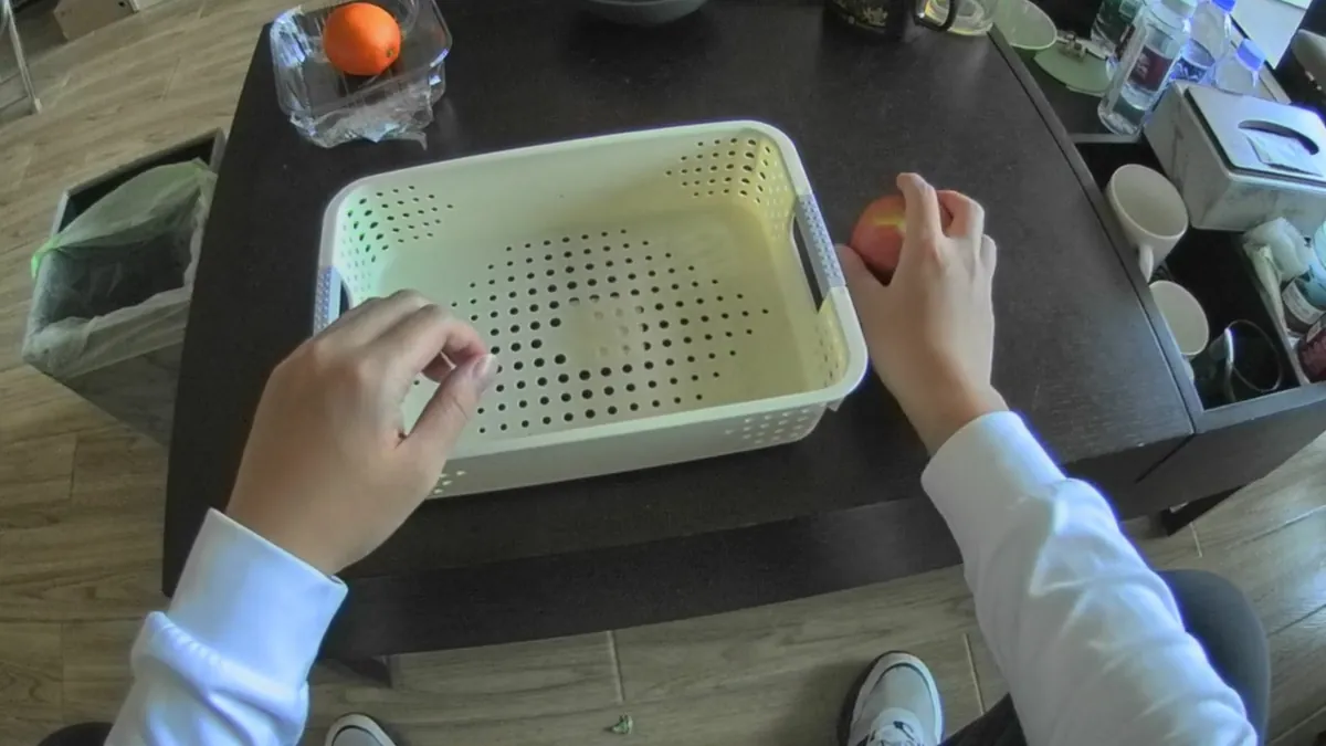 Head-mounted view of hands putting an apple into a basket on a table