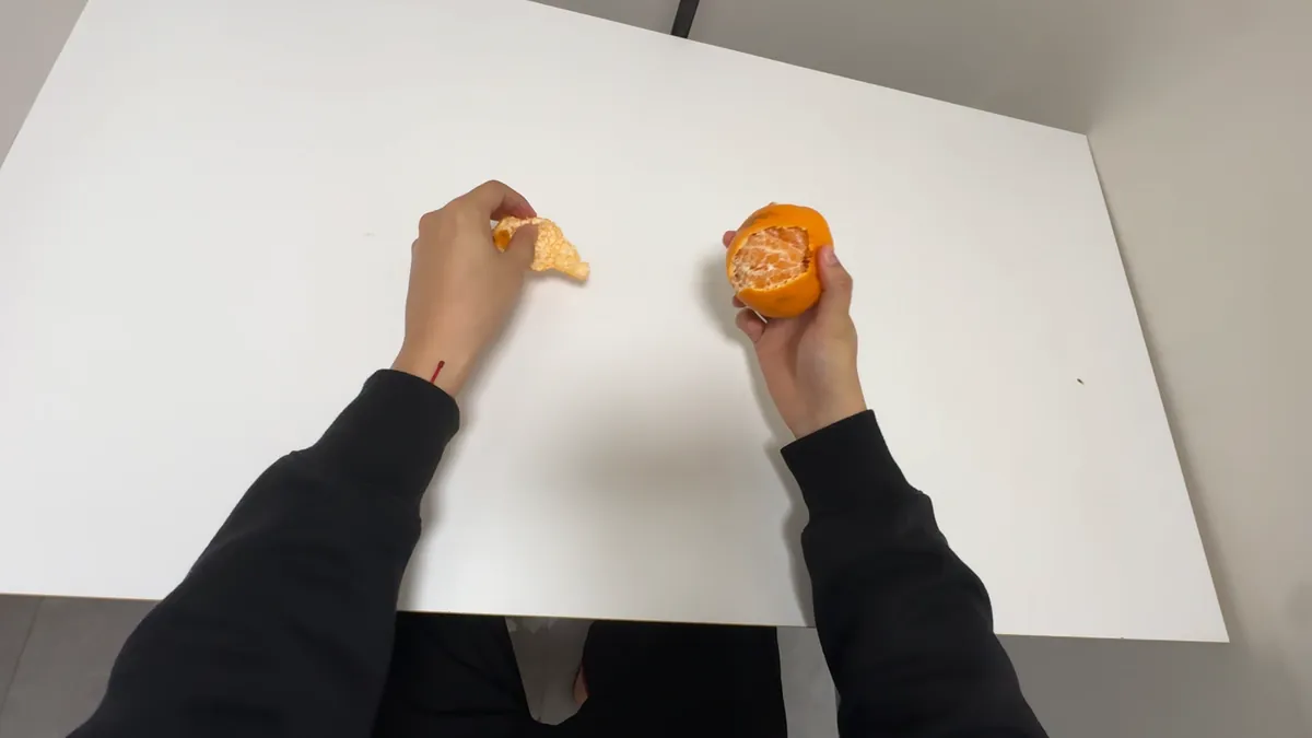 Head-mounted view of two hands peeling an orange over a white table