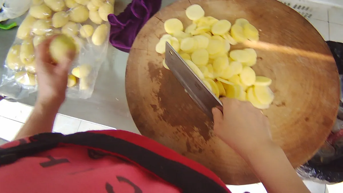 Head-mounted view of hands slicing potatoes on a round chopping board