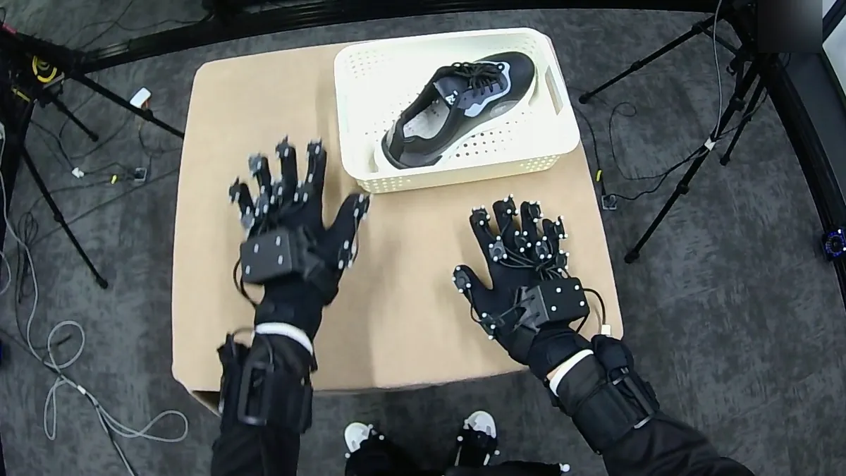 Head-mounted view of two marker-tracked gloves reaching for a shoe in a basket inside a capture rig