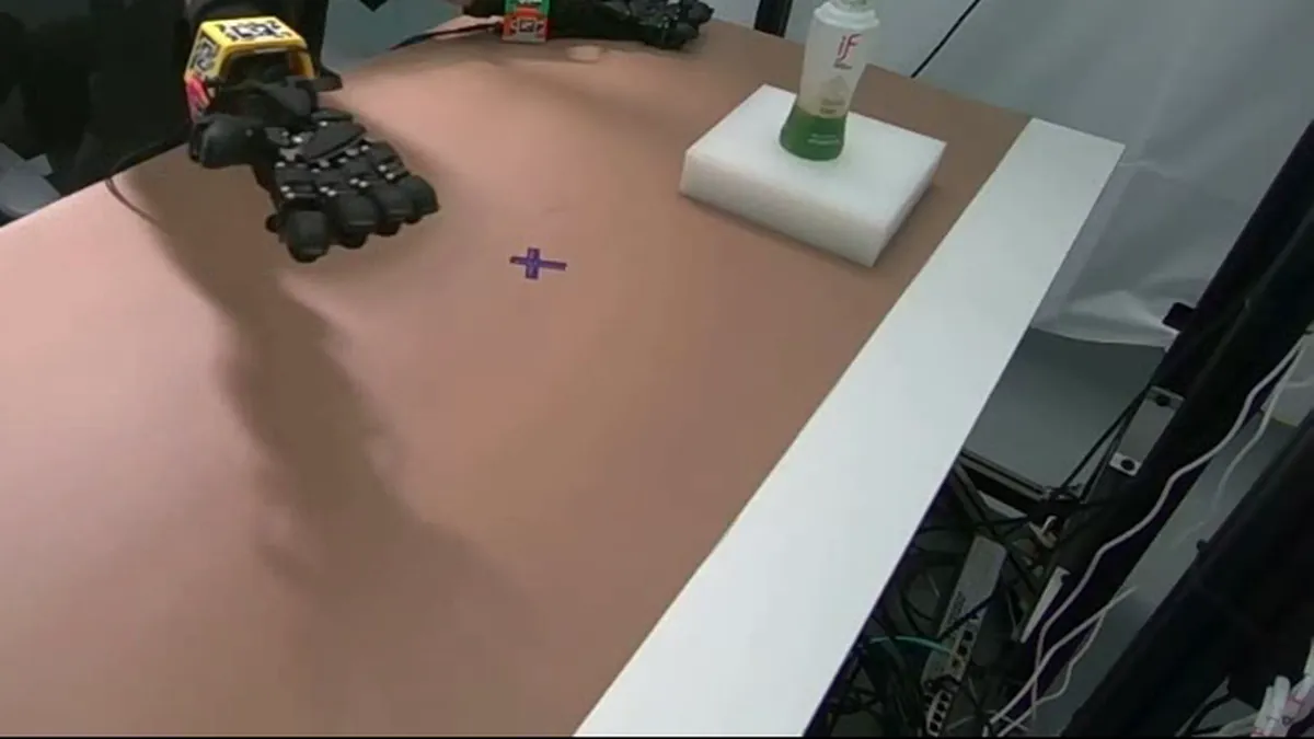 Fixed camera view of a tactile glove reaching across a table toward a bottle