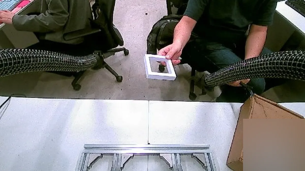 Base camera view of a soft continuum arm receiving a small frame handed over by a person