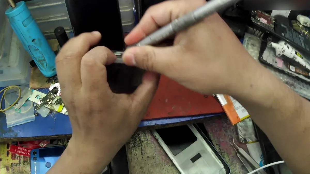 Head-mounted view of hands working on a phone with a precision tool at a repair bench